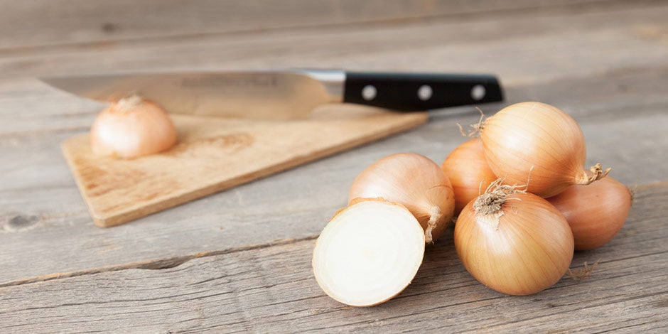 Qué verduras pueden comer los perros-Cebolla Cebolla cortada junto a un cuchillo. Hace parte de las verduras que no pueden comer los perros.