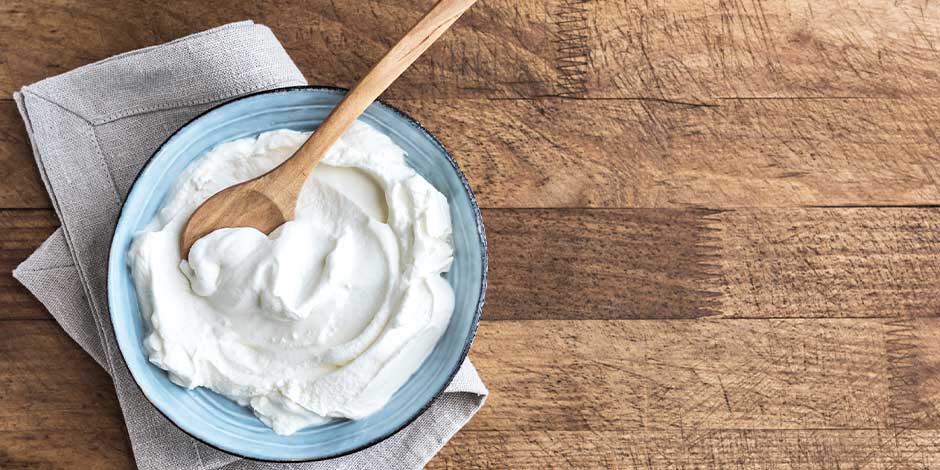 Los perros pueden comer yogur griego - Recipiente Los perros pueden comer yogur griego. Recipiente junto a cuchara.