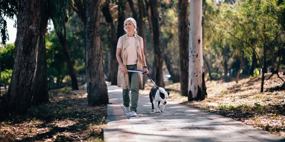 Mujer adulta paseando en medio de un parque en compañía de su mascota blanco con negro. Aprendé cuánto vive un perro y disfrutá más con él.